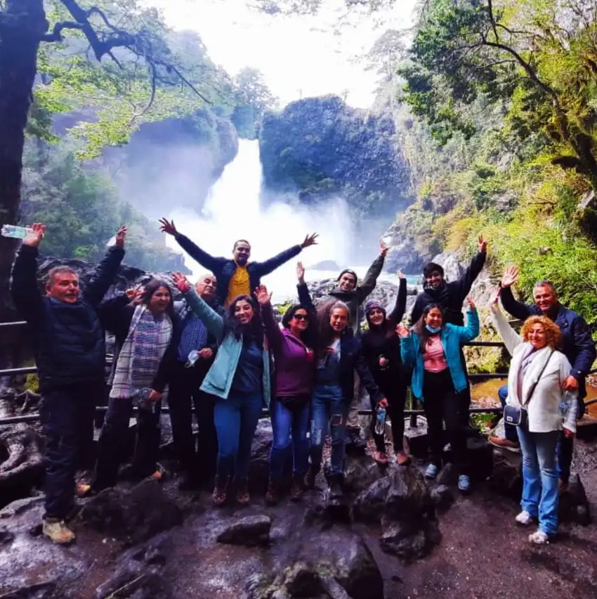 Grupo de turistas celebrando frente a un salto de agua en la Reserva Huilo Huilo, tour desde Pucón
